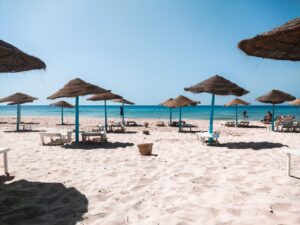 Peaceful sandy beach with straw umbrellas and clear blue sea under a bright sky.